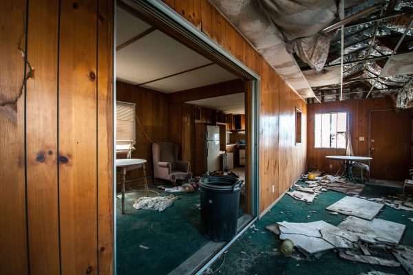 A derelict wooden-walled dwelling in an advanced state of disrepair, its roof and supporting walls torn apart and its floors worn down